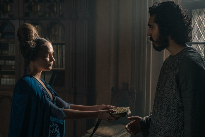 Alicia Vikander gives book to Dev Patel in The Green Knight