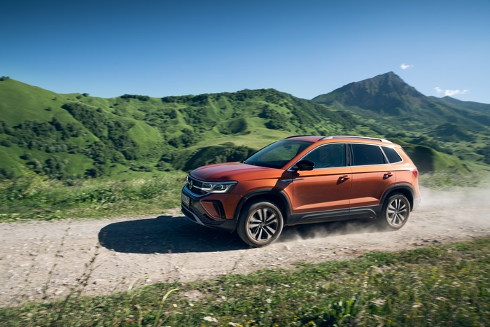 Orange Volkswagen Taos SUV driving through green mountains