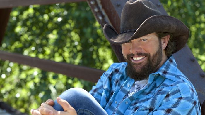 Toby Keith smiling in cowboy hat and blue plaid shirt