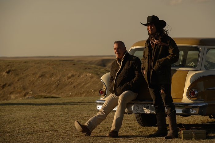 Kevin Costner and Booboo Stewart by vintage car in western landscape