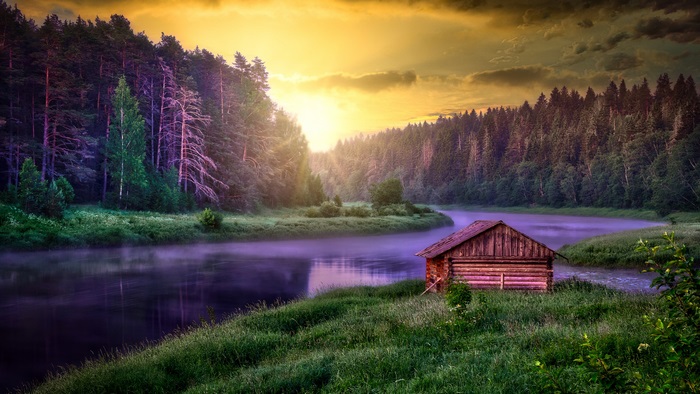 Golden sunset light on a cabin by a misty river