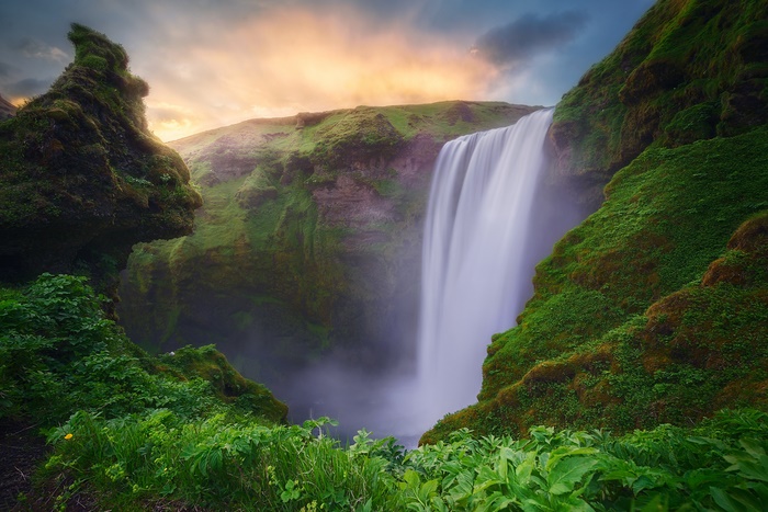 Majestic waterfall cascading down moss-covered cliffs at sunset