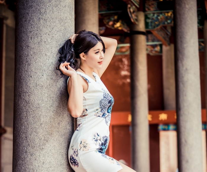 Asian woman in floral dress posing by column
