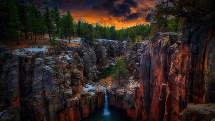 Canyon with waterfall and forest at sunset