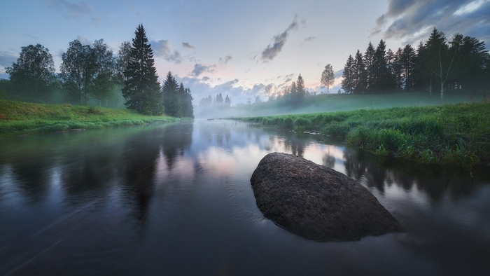 Misty river at sunrise with a large rock