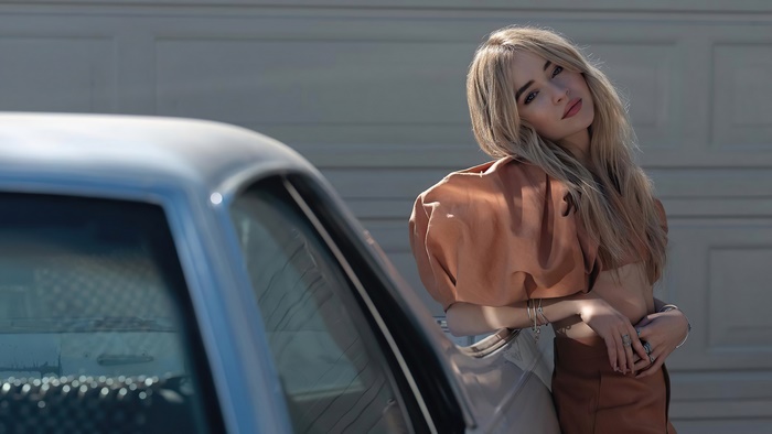 Sabrina Carpenter leaning on a car