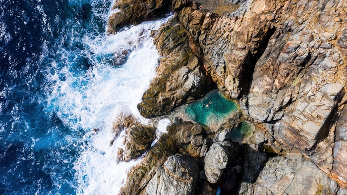 Aerial view of a person swimming in a rock pool by the ocean