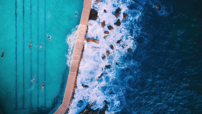 Aerial view of people swimming in a pool next to the ocean