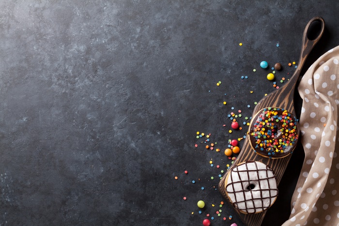 Two donuts with sprinkles and chocolate on a wooden board