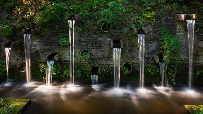 Stone wall with multiple waterfalls and greenery