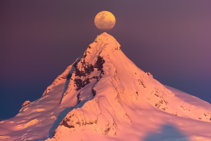 Moon over snow-covered mountain peak at sunset