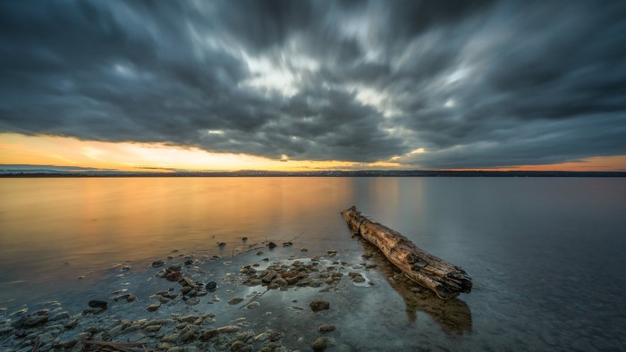 Sunset over the sea with dramatic clouds and driftwood