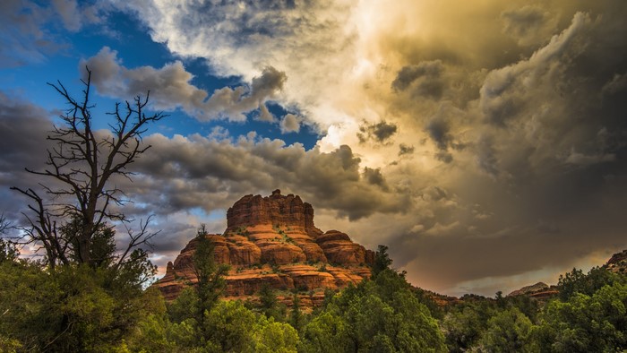 Red rock formation with dramatic clouds and dead tree