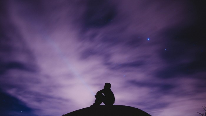 Silhouette of a person sitting on a hill under a starry sky