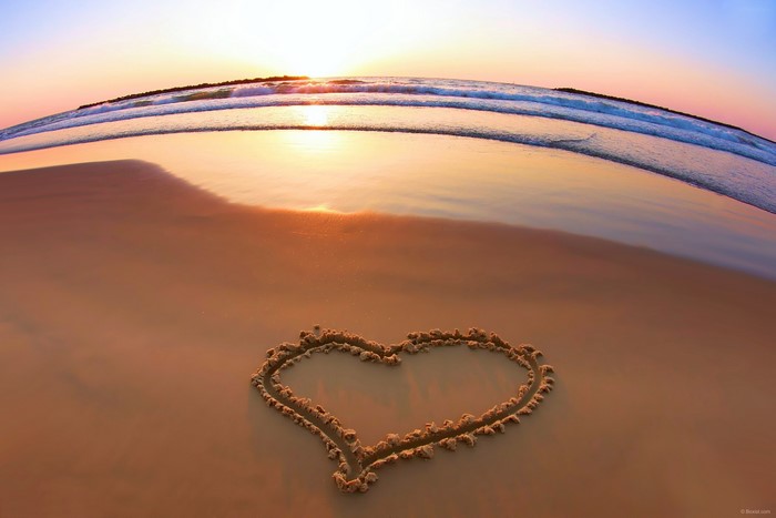 Heart drawn in sand on a beach at sunset
