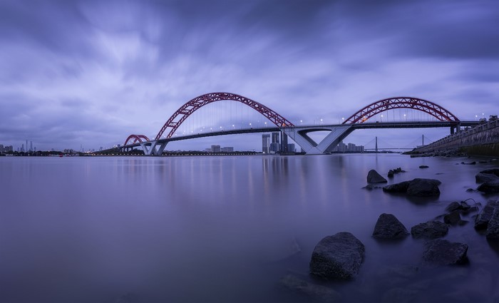 Arched bridge over water at dusk with city skyline