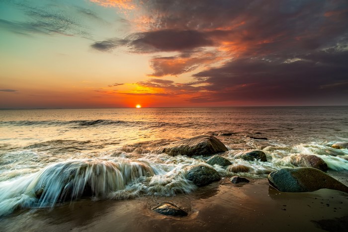 Sunset over the sea with waves crashing on rocks