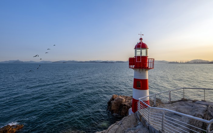 Red and white lighthouse on rocks by the sea with birds