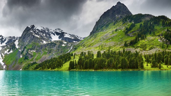 Turquoise lake with snow-capped mountains and green forest