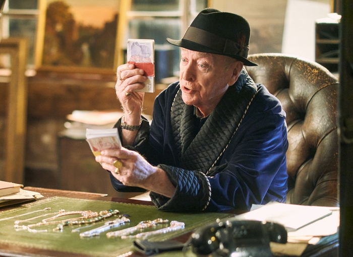 Michael Caine counting money in a blue robe