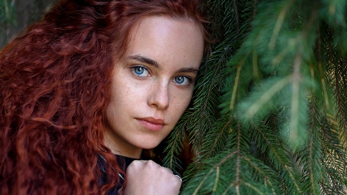 Young redhead woman with blue eyes near pine tree