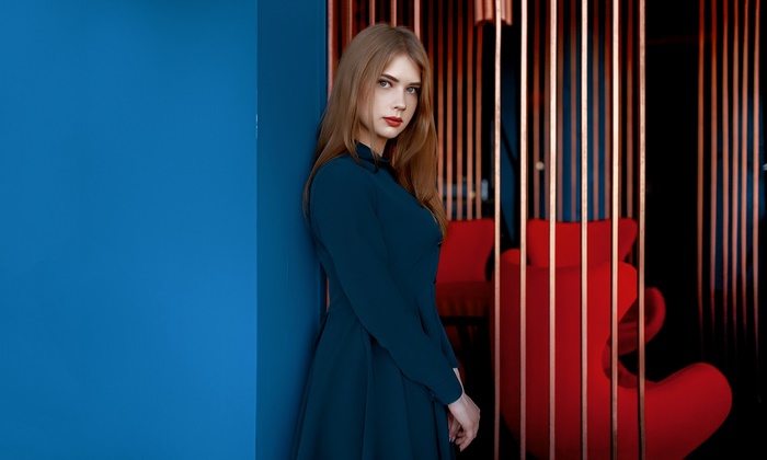 Woman in a blue dress leaning against a blue wall