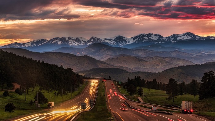 Time-lapse of a highway leading to snow-capped mountains at sunset