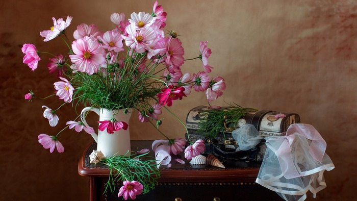 Pink cosmos flowers in a white pitcher with a decorative chest