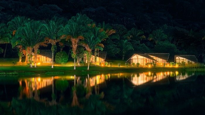 Night view of bungalows by the lake with palm trees