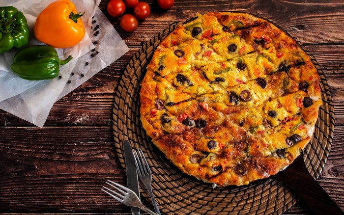 Round pizza with olives and bell peppers on a wooden table