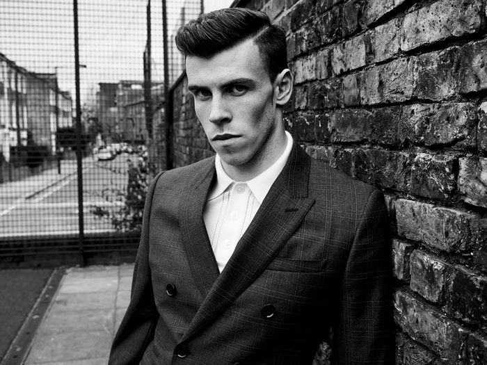 Gareth Bale in a suit leaning against a brick wall
