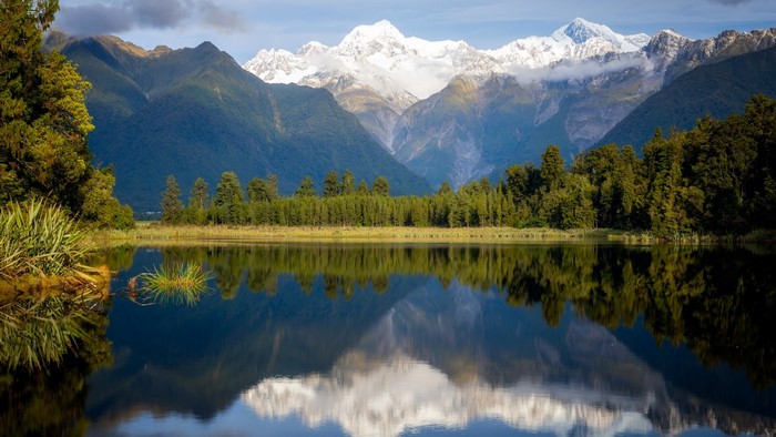 Snowy mountains reflected in a calm lake with trees