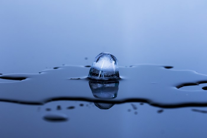 Melting ice cube on water with reflection