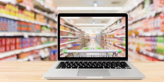 Laptop displaying a shopping cart in a supermarket aisle