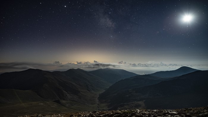 Mountains under starry sky with moon and clouds