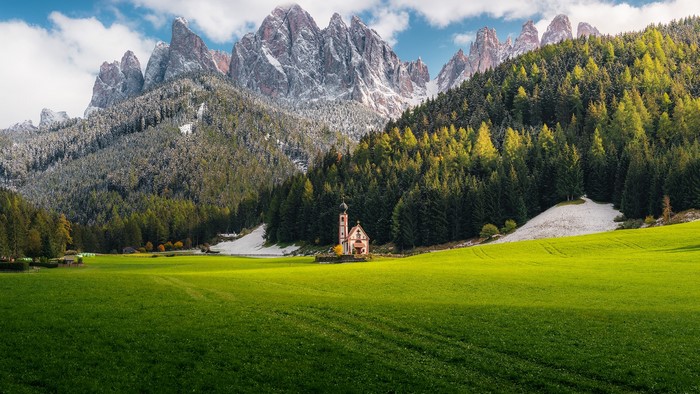 Church in a green field with snowy mountains