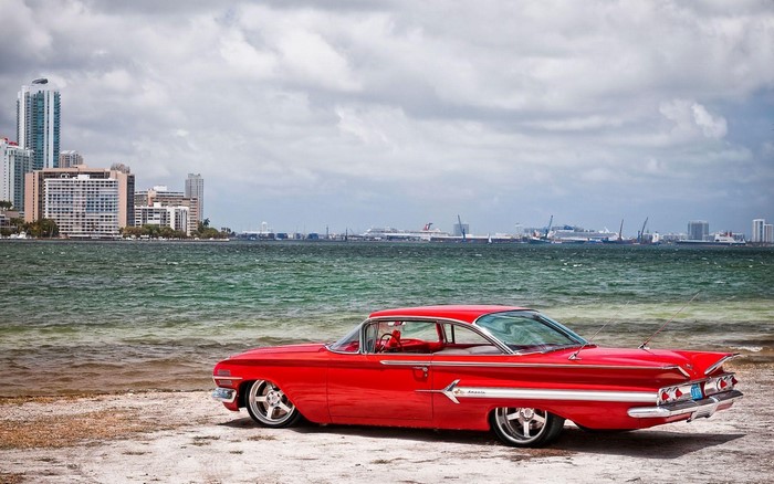 Red classic car on a beach with city skyline