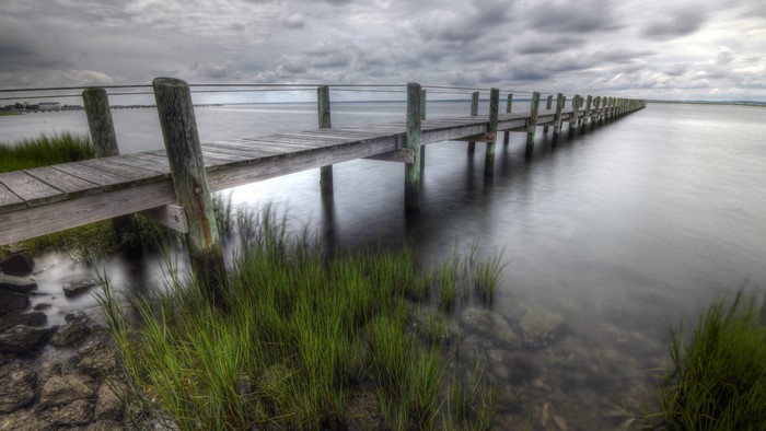 Wooden pier extending into a calm body of water under a cloudy sky