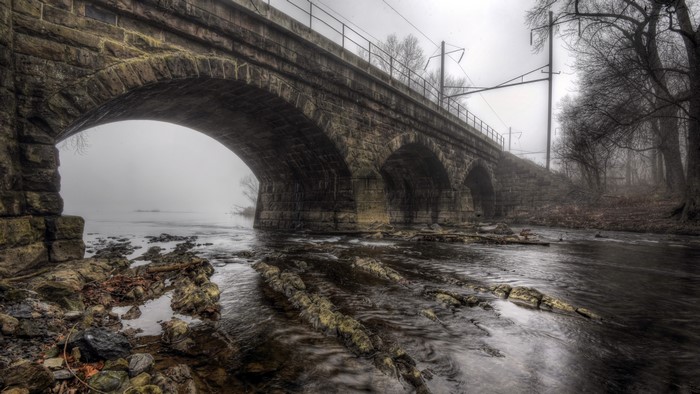 Old stone bridge over a river in fog