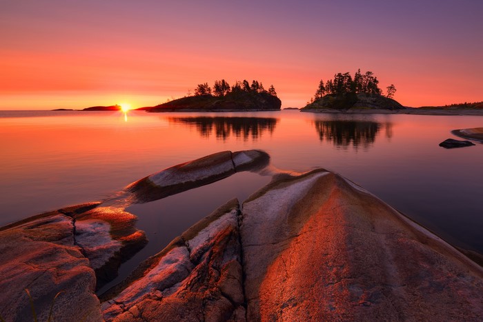 Sunrise over a calm lake with islands and rocks