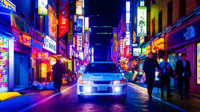 White Mitsubishi Lancer Evo V on a neon-lit street in Japan at night