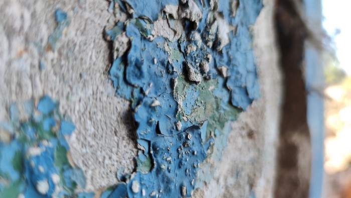 Peeling blue paint on a concrete wall outdoors