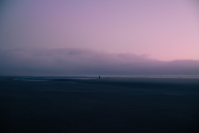 Person walking on a foggy beach at sunset