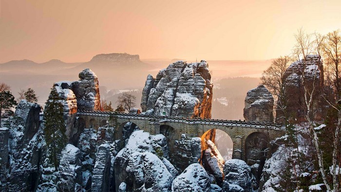 Snow-covered rock formations with a bridge at sunrise