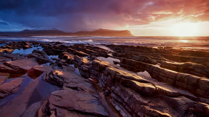 Rocky coastline at sunset with mountains in the distance
