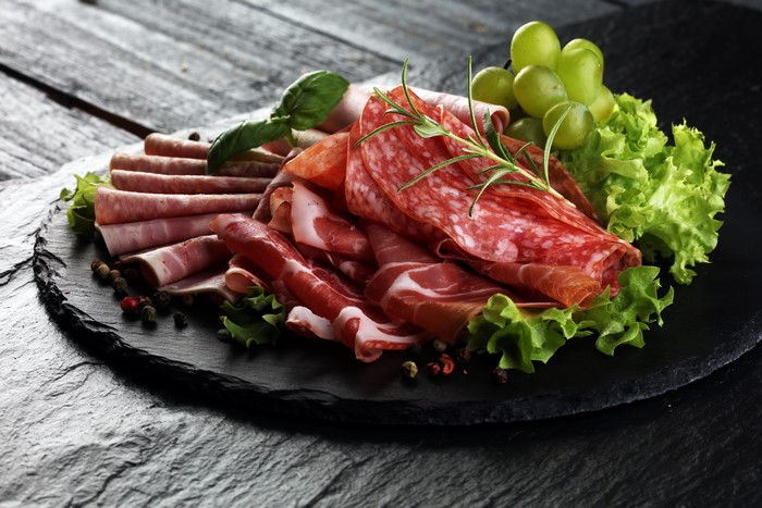 Charcuterie board with salami, prosciutto, grapes, and herbs