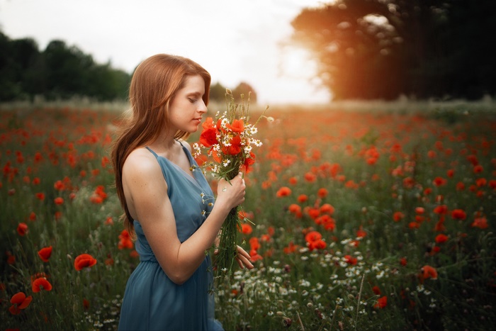 Redhead in blue dress smelling poppies in a field