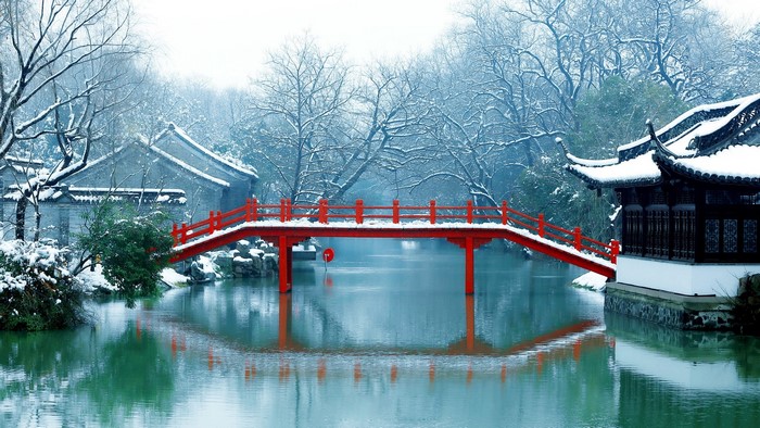 Red bridge over water in a snowy Chinese garden