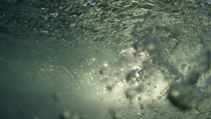 Underwater view of sunlight filtering through waves and bubbles