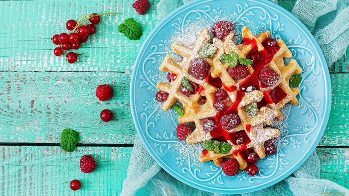 Waffles with raspberries and red currants on a cyan plate